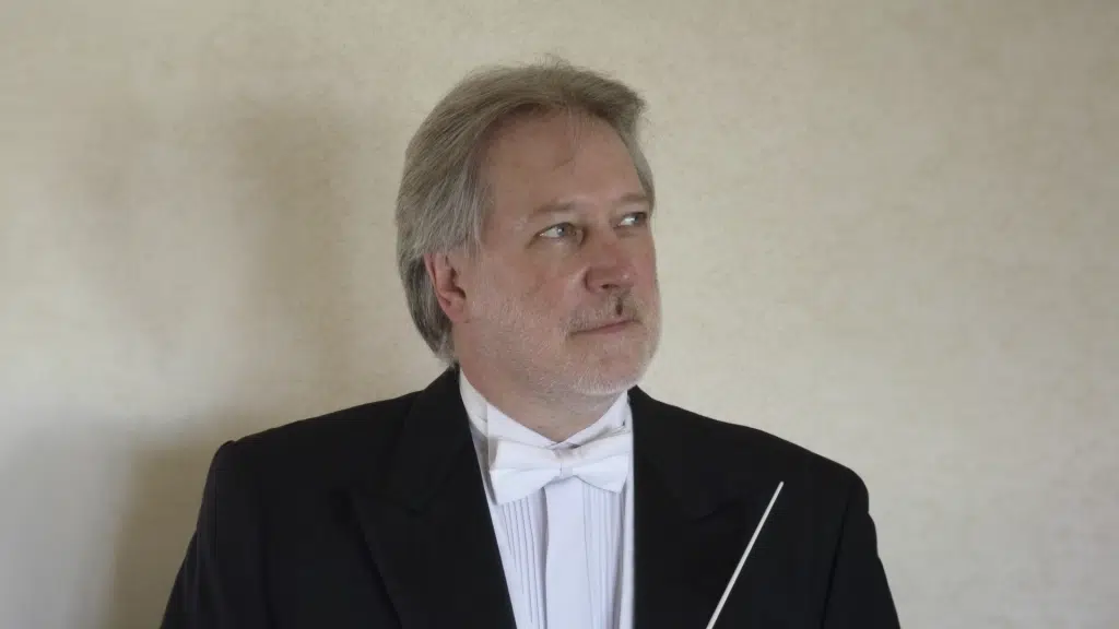 A photo of Colin Touchin (a white man with grey hair) in a tuxedo against a beige background.